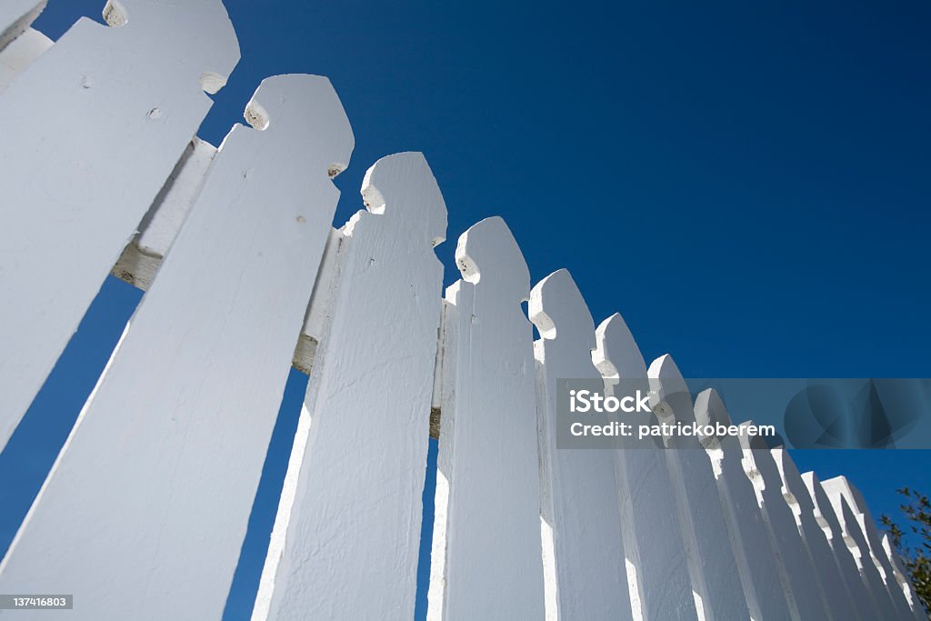Worm's-eye view of white picket fence and blue sky White picket fence in suburbia. Fence Stock Photo