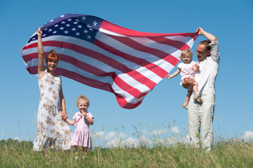Happy family with two children on meadow. Women and man holding large American Flag