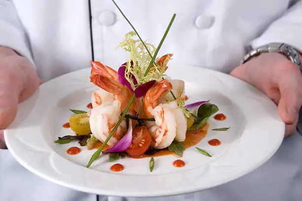 A shrimp dish with a chef handling it.
