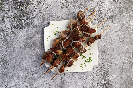 Shish kebabs on a wooden skewers on a white square  plate on a dark background. Top view, flat lay