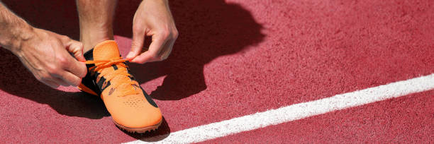 tênis de corrida na linha de início sucesso desafio bandeira competição. atleta homem em forma se preparando para corrida de corrida amarrando tênis de corrida. panorâmico em trilhas de tartan vermelho. - track and field stadium - fotografias e filmes do acervo