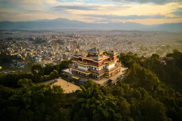Elevated perspective of Pullahari Monastery, Buddhist pilgrimage site on northern hill in Kathmandu Valley with city and mountains in background.