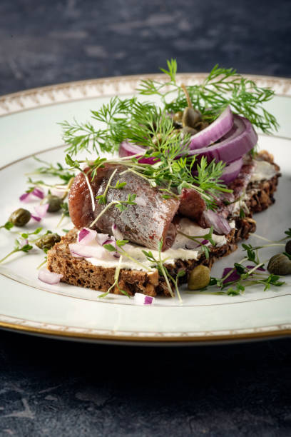 Traditional danish “smørrebrød” or open sandwich made with a slice of buttered rye bread, marinated herring, shavings of horseradish and topped with red onion, fresh dill and capers. Colour, vertical format with some copy space. Smorrebrod are a staple of the danish food culture, a very popular choice for lunch or a light dinner. Toppings can be almost anything from roast beef to prawns but the rye bread at the bottom of the sandwich has to be good!