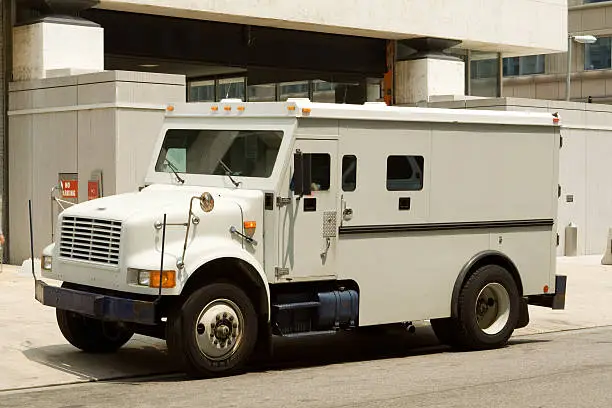 Side view of gray armored truck parked on street making a cash pickup. - See lightbox for more