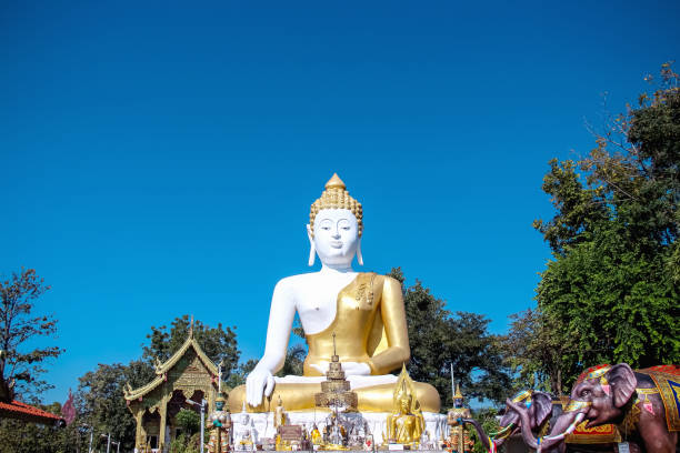 istock Sitting Buddha image on bright blue sky view background at  phra that doi khum  temple in Chiang Mai of Thailand 1374293198