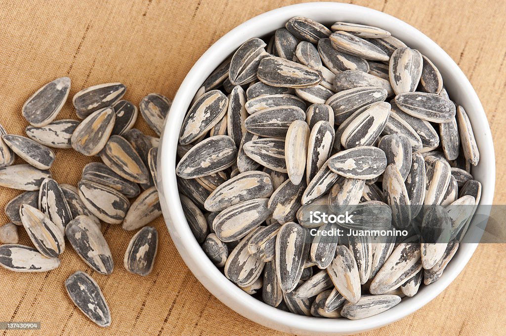 A Bowl Overflowing With Sunflower Seeds in the Shells Small bowl of sunflower seeds on white background Bowl Stock Photo