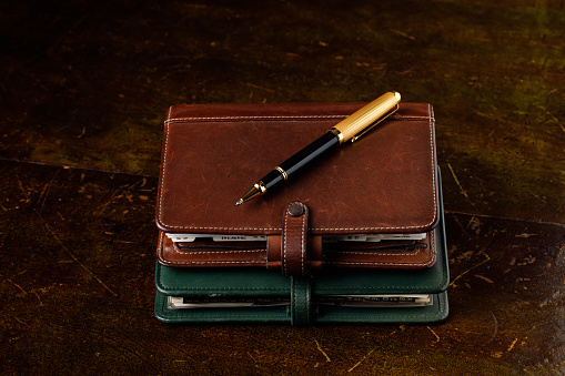 Brown and green leather diaries and a black and gold pen on an old desk.
