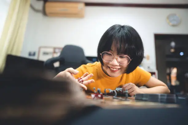 People lifestyle with interesting hobby at home concept. Young adult asian woman playing board game on top table. Hand holding dice roll. Happy with smile face.