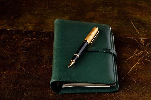 Green leather diary and pen on an old desk.