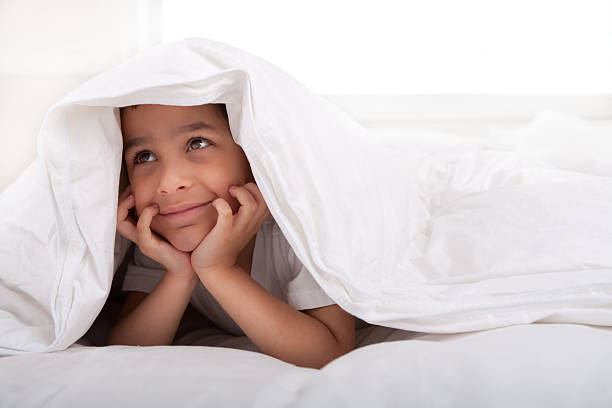 Smiling little boy laying under blanket
