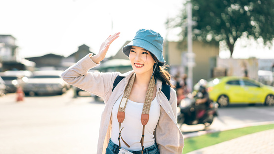 Walking young adult southeast asian woman traveller wear blue hat and backpack. People traveling in city lifestyle at outdoor with sunlight. Staycation summer trip concept.