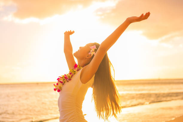 hawajska tancerka hula kobieta nosząca naszyjnik z kwiatów lei na plaży o zachodzie słońca tańcząca z otwartymi ramionami za darmo o zachodzie słońca relaksująca się na hawajskich wakacjach podróżniczych. azjatycka dziewczyna ze świeżymi kwi - hawajczyk ethnicity zdjęcia i obrazy z banku zdjęć