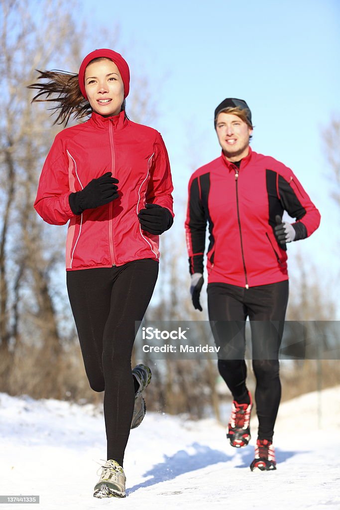 Couple running in winter snow Sport couple running in winter snow. xwoman and man runners jogging outdoors. Healthy fitness lifestyle concept with happy smiling young multiracial couple. Winter Stock Photo