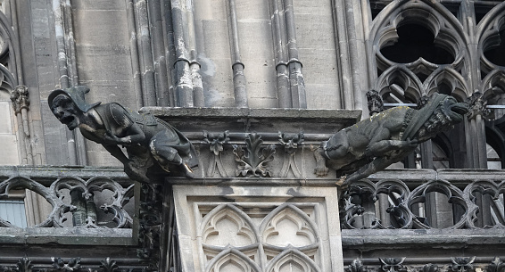 A witch at the left and and monster at the right. A gargoyle is a sort of demon or devil with a spout designed to convey water from a roof and away from the side of a building, thereby preventing rainwater from running down masonry walls and eroding the mortar between.