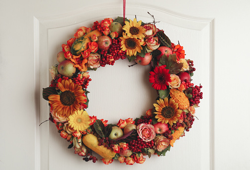 Beautiful autumnal wreath with flowers, berries and fruits hanging on white wooden door. Space for text