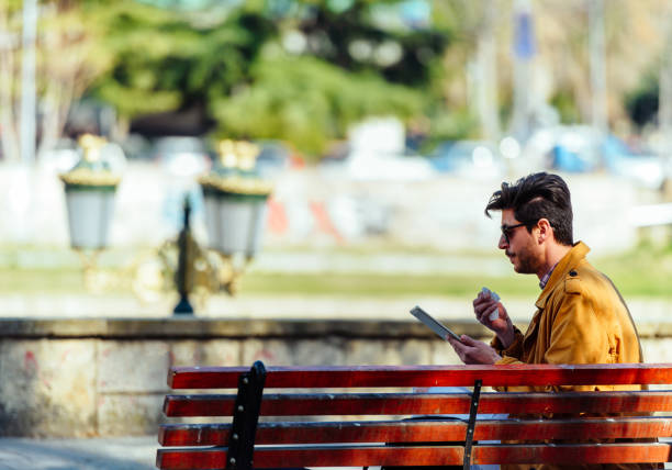 Well dressed businessman is sitting in the park and working on his PC tablet