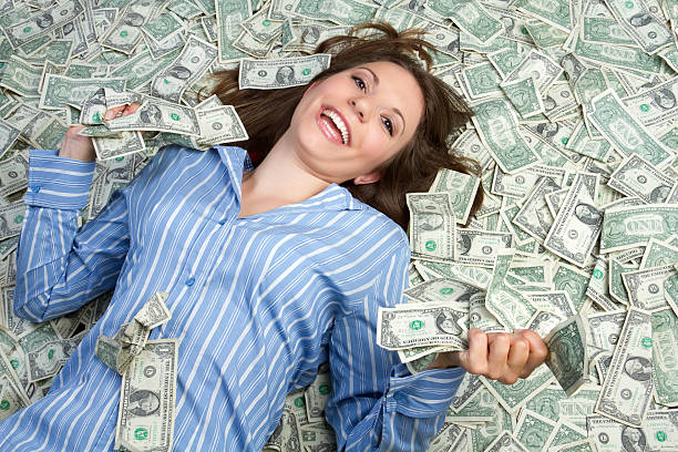 Woman in blue shirt smiling while lying in money stock photo