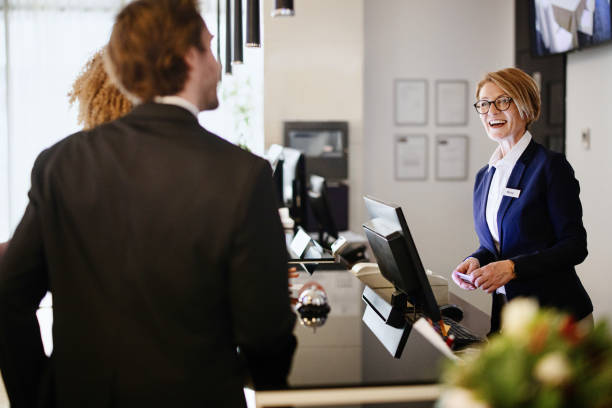 Multi-ethnic business couple arriving at hotel reception desk Female hotel receptionist helping a business couple guests in checking in process. Hotel receptionist assisting guests for checking in concierge photos stock pictures, royalty-free photos & images
