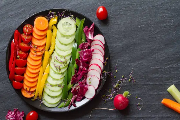 Photo of Fresh sliced vegetables in rainbow colors on black background, healthy diet concept