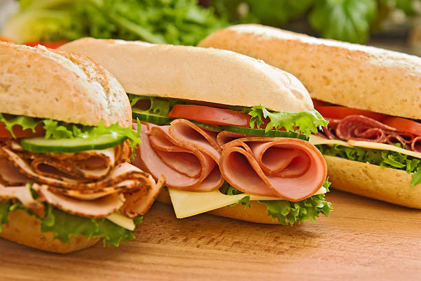 Turkey/chicken breast, ham & swiss and salami sandwiches Three fresh sub sandwiches - turkey/chicken breast, ham & swiss and salami on a cutting board. Focus on the ham sandwich submarine sandwich photos stock pictures, royalty-free photos & images
