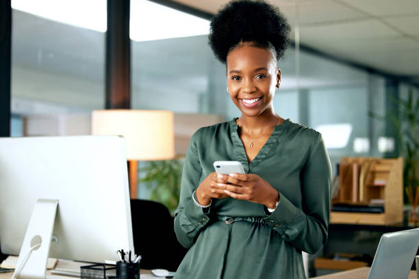 Shot of a young businesswoman using a phone in an office at work Social media keeps me updated on the latest news black business woman stock pictures, royalty-free photos & images