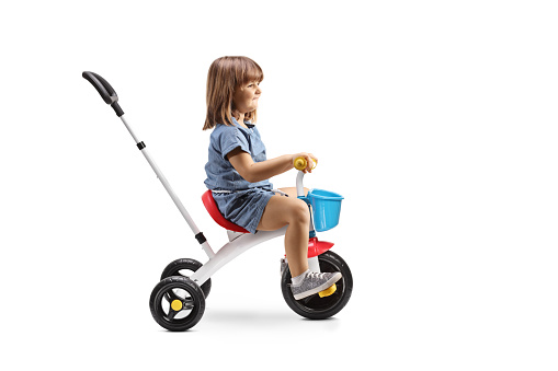 Profile shot of a girl riding a tricycle isolated on white background