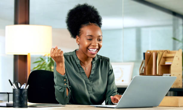 shot of a young businesswoman cheering while using a laptop in an office at work - excitement business person ecstatic passion imagens e fotografias de stock