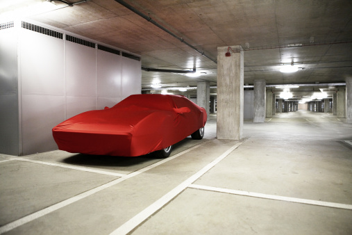 A sports car covered up in bright red  material in an empty underground Car Park.Automotive or maybe Economic Downturn Concept.