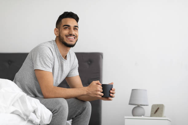istock Start Of The Day. Arab Guy Sitting On Bed And Drinking Coffee 1374576007