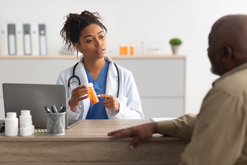 istock Female black doctor showing pills to male patient 1374578120