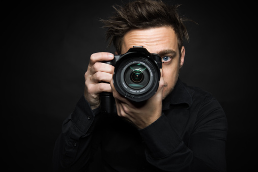 Mature man taking a photo of a young man with a professional camera isolated on white background