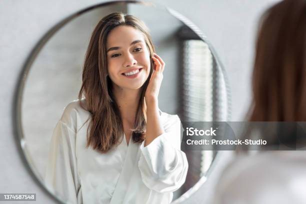 Beauty Concept Portrait Of Attractive Happy Woman Looking At Mirror In Bathroom Stock Photo - Download Image Now