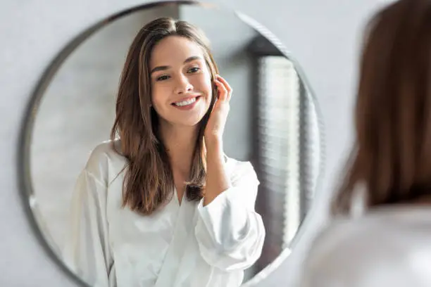 Photo of Beauty Concept. Portrait Of Attractive Happy Woman Looking At Mirror In Bathroom
