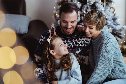Beautiful happy young family smiling and embracing in front of a Christmas tree in the living room
