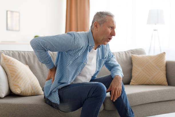 istock Mature man with side back pain sitting on couch at home 1374589187
