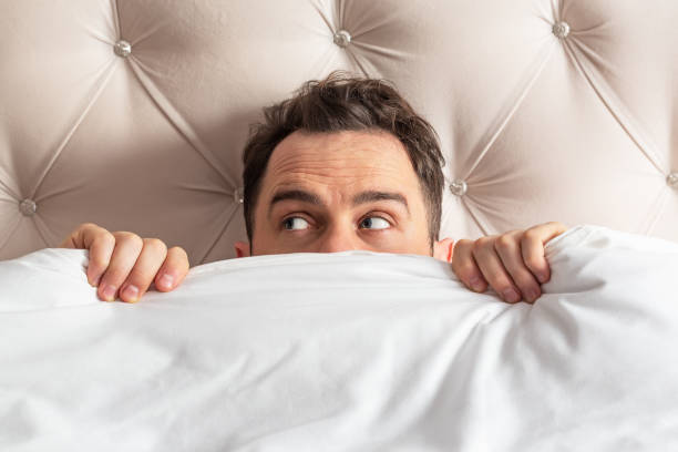 istock Caucasian young man hiding in bed under the blanket at home. 1374600519