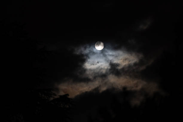 close up view of the full white moon being covered by the clouds in the dark sky at night
