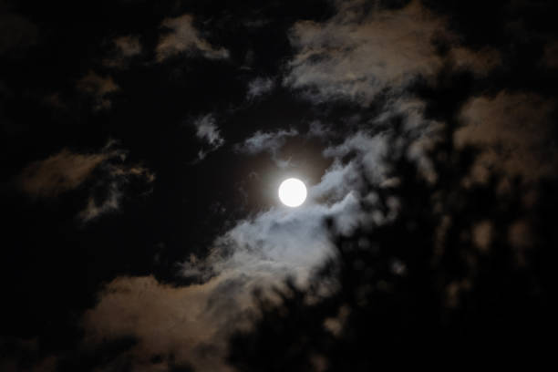 full white moon seen from behind little clouds at night in the dark sky