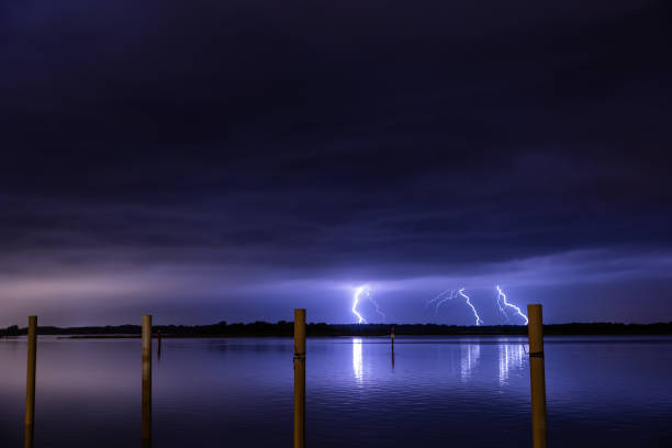 hermosos rayos púrpuras y azules que golpean poderosamente lejos en la tierra por la noche durante una tormenta en verano - low key lighting flash fotografías e imágenes de stock