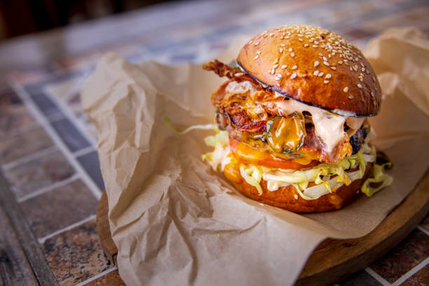 Bacon cheeseburger with salad in bun on wrapping paper, served on wooden board on bar table
