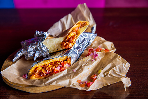 Burritos filled with meat and vegetables wrapped in aluminum foil, served on wrapping paper on restaurant table