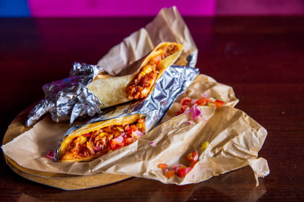 Burritos filled with meat and vegetables in aluminum foil on restaurant table Burritos filled with meat and vegetables wrapped in aluminum foil, served on wrapping paper on restaurant table burrito wrap stock pictures, royalty-free photos & images