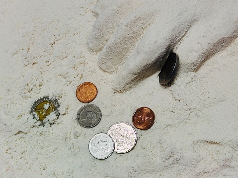 Hand Finding Money Coins in The Sand.