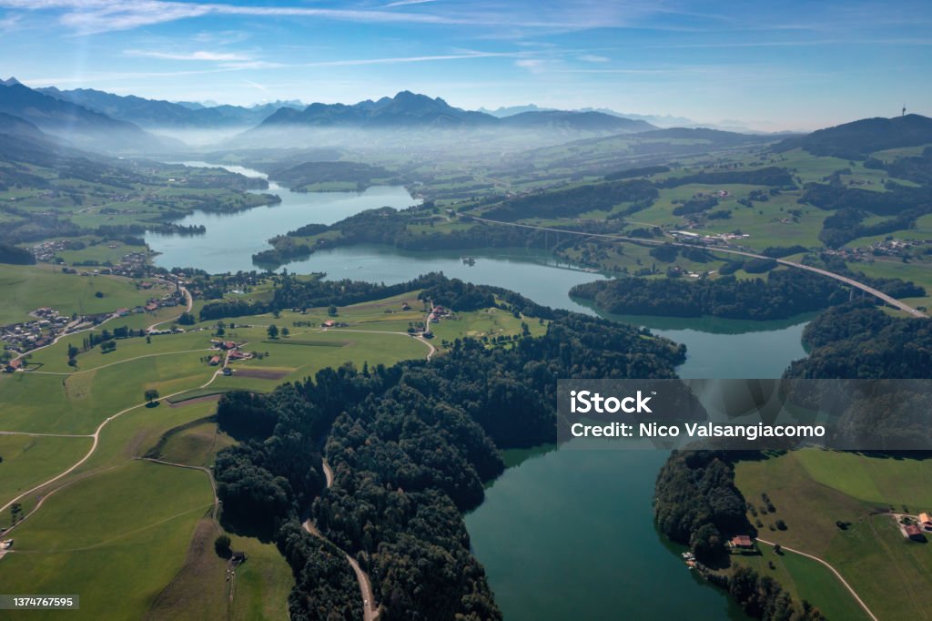 Aerial view of the Lac de la Gruyere, a lake in the canton of Fribourg, Switzerland. The lake winds through the hills of the region and is surrounded by a layer of trees. Aerial view of the Lac de la Gruyere, a lake in the canton of Fribourg, Switzerland. The lake winds through the hills of the region and is surrounded by a layer of trees. High quality photo. Gruyeres Stock Photo