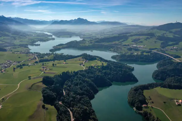 Aerial view of the Lac de la Gruyere, a lake in the canton of Fribourg, Switzerland. The lake winds through the hills of the region and is surrounded by a layer of trees. High quality photo.