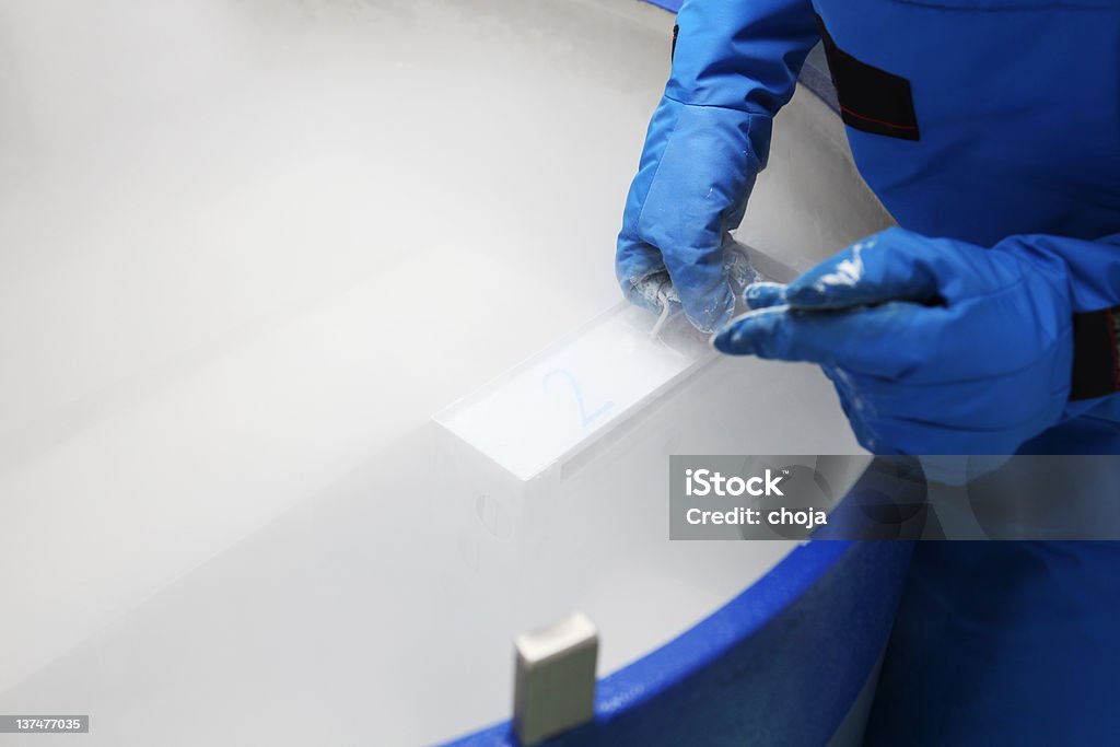 Contenitore con il liquido nitrogen.doctor con tuta hazmat al lavoro - Foto stock royalty-free di Criobiologia