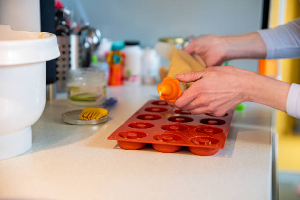 istock Woman in Domestic Kitchen Pouring Donuts Dough into Molds 1374788019