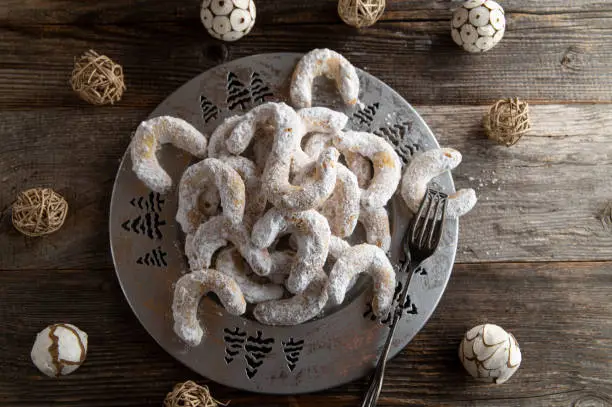 Traditional german christmas cookies called vanillekipferl. Served on a silver plate with decoration on dark wooden table background. Overhead view with copy space