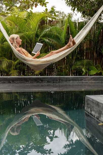 Woman relaxing in an hammock by the pool with a digital tablet