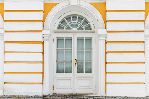 Old white wooden door in yellow wall, background texture. Classic architecture details